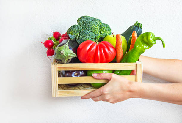 Woman holding crate of fresh vegetables on white background. Healthy eating and dieting. Fast contactless delivery and shopping online.